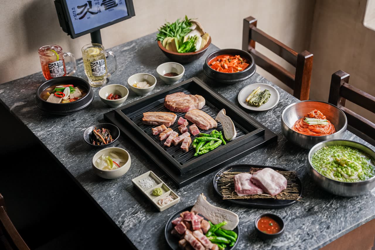 매장 자리에 실제로 차려진 상. 화로가 놓인 테이블 위로 고기 접시와 반찬이 놓이고, 뒤로 나무 의자와 벤치가 보인다