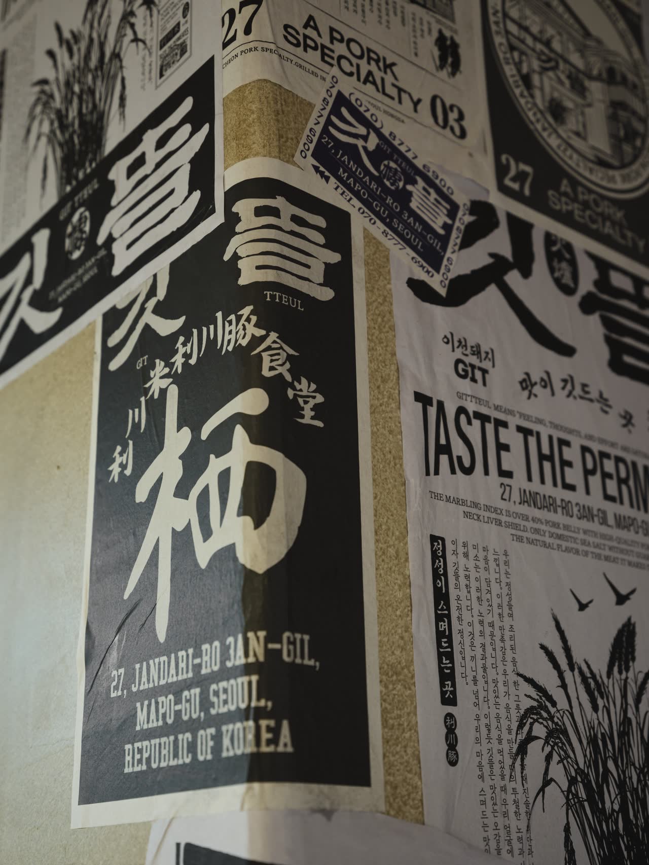 깃뜰 활자 포스터를 겹쳐 붙인 벽. 'A PORK SPECIALTY 03', '利川豚 食堂', 그리고 '27, JANDARI-RO 3AN-GIL, MAPO-GU, SEOUL, REPUBLIC OF KOREA'라는 주소가 함께 인쇄되어 있다